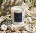 Bougie Musc blanc JLT présentée avec du coton et des fleurs blanches dans une ambiance lumineuse