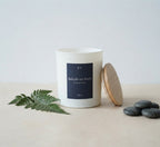 Bougie parfumée Balade en forêt JLT en cire végétale, présentée avec fougère, galets et couvercle en bois.