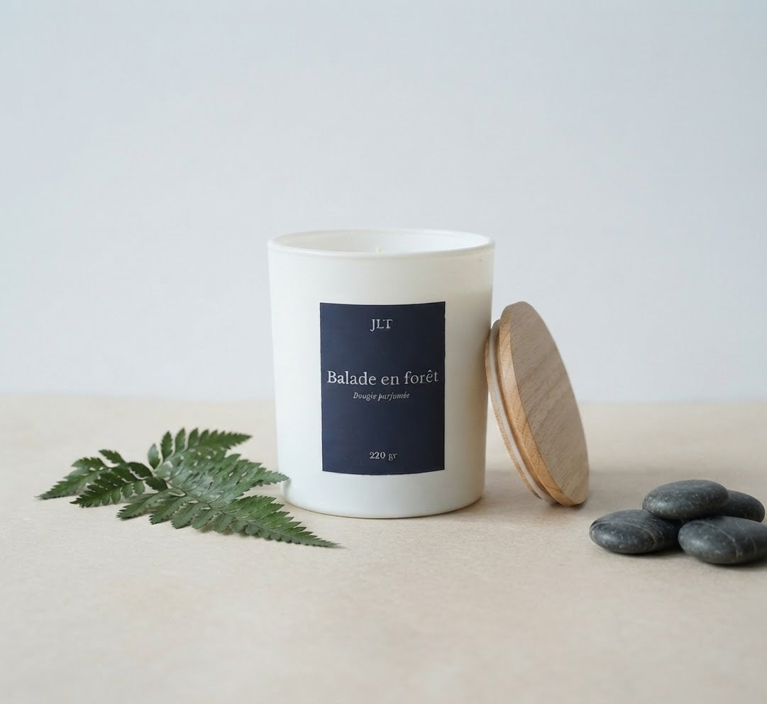 Bougie parfumée Balade en forêt JLT en cire végétale, présentée avec fougère, galets et couvercle en bois.