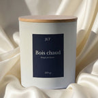 Bougie parfumée Bois chaud JLT 220g en verre blanc mat avec étiquette bleu nuit  en ambiance lumineuse sur drap ivoire