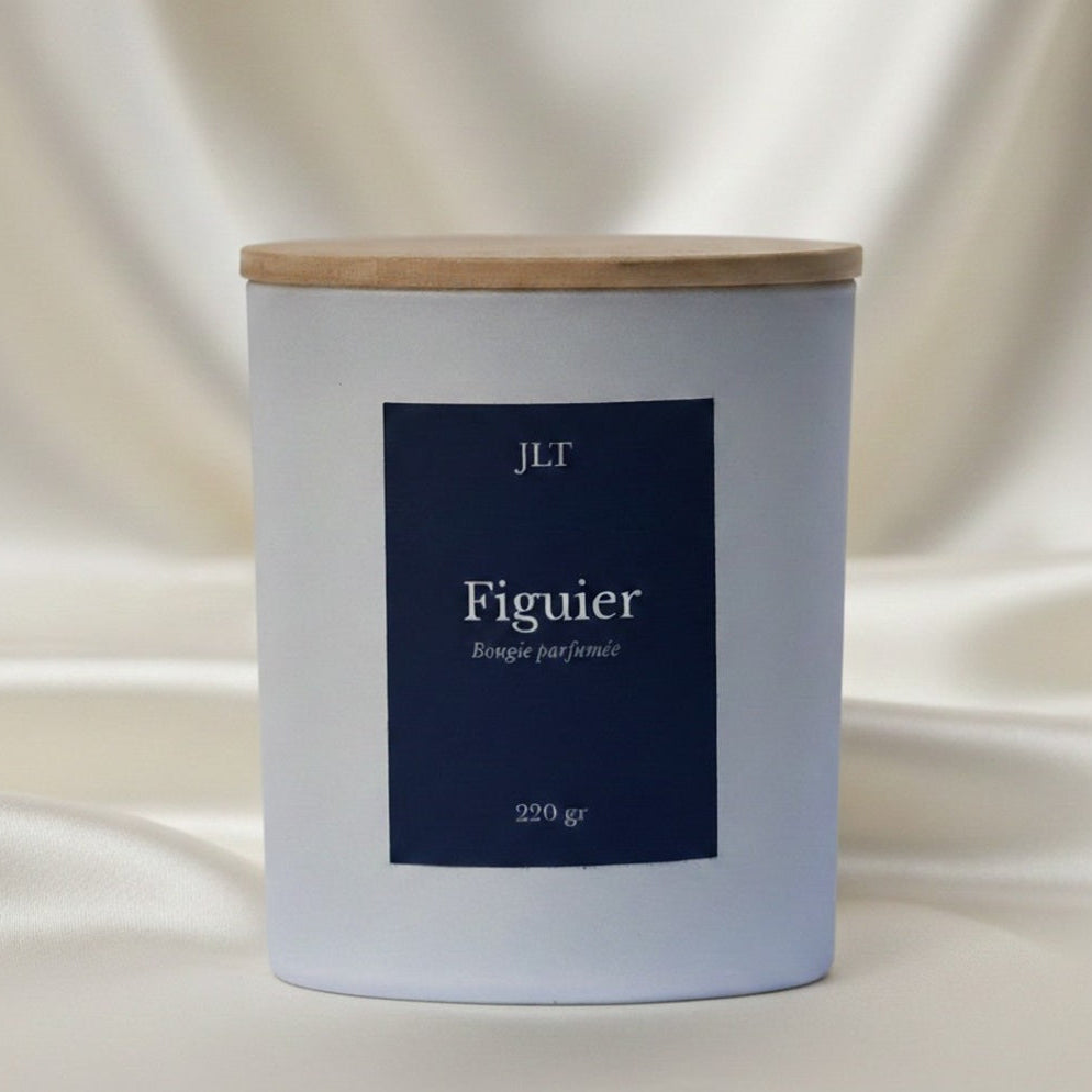 Bougie parfumée Figuier JLT en verre blanc mat étiquette bleu nuit dans une ambiance lumineuse sur drap ivoire