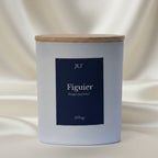 Bougie parfumée Figuier JLT en verre blanc mat étiquette bleu nuit dans une ambiance lumineuse sur drap ivoire