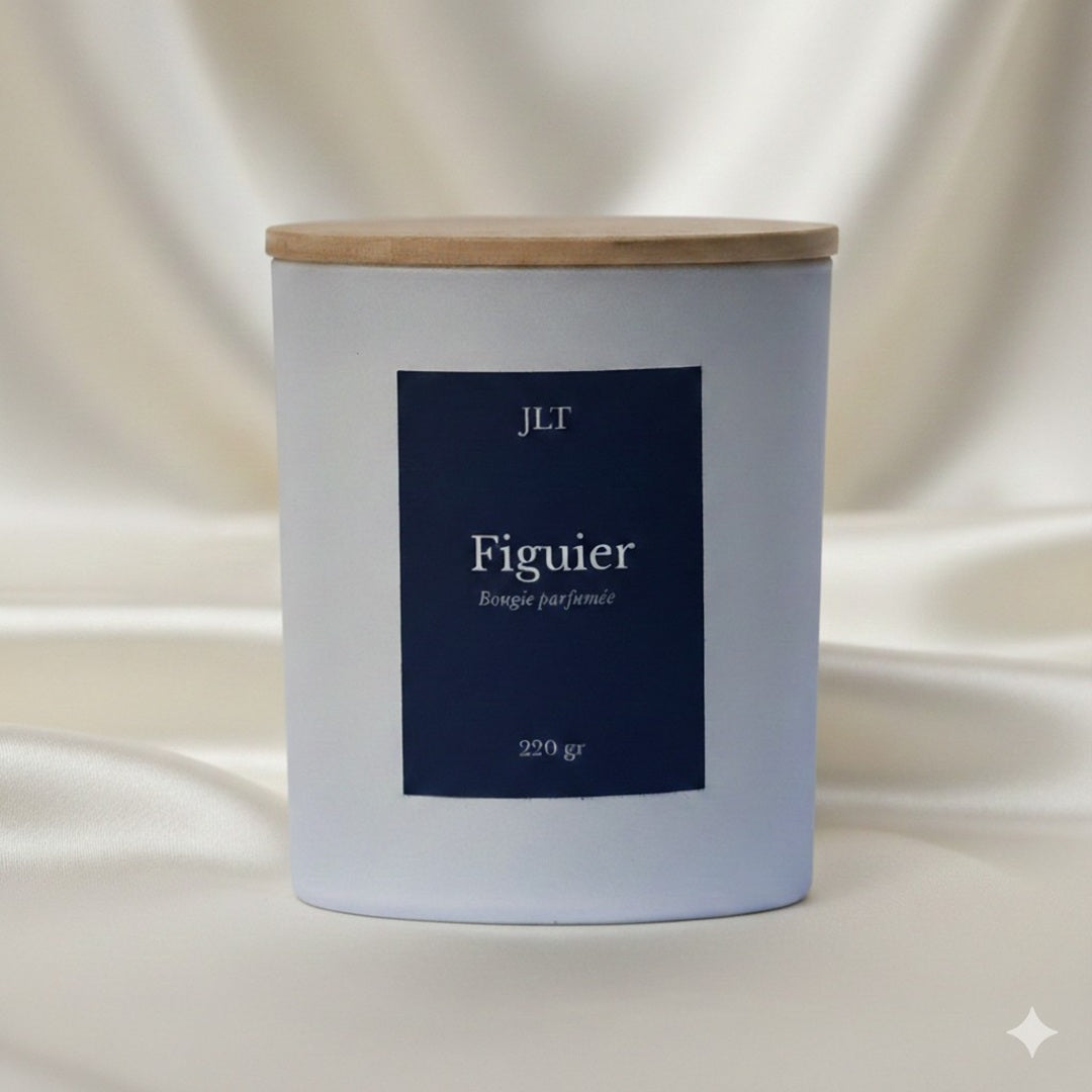Bougie parfumée Figuier JLT en verre blanc mat étiquette bleu nuit dans une ambiance lumineuse sur drap ivoire
