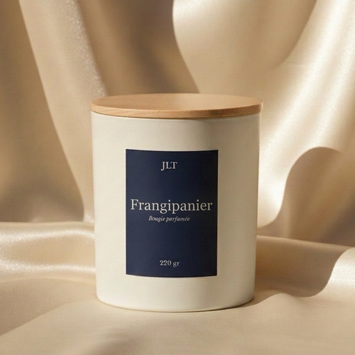 Bougie parfumée frangipanier JLT 220g posée sur un tissu satiné, ambiance douce et élégante, décoration intérieure lumineuse