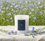 Bougie parfumée Lin JLT 220 g présentée parmi des fleurs bleues dans une ambiance fraîche et naturelle