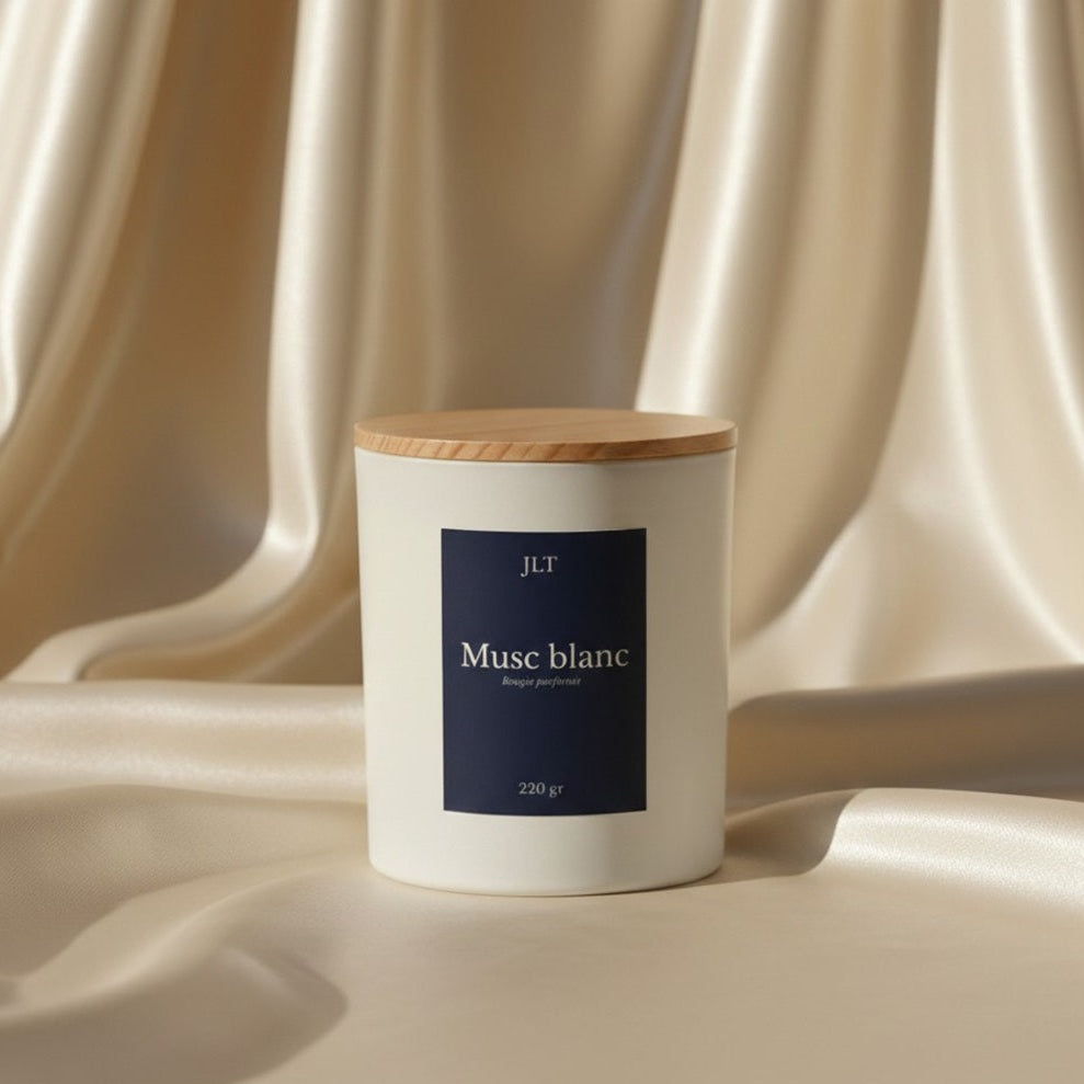 Bougie parfumée Musc blanc JLT en verre blanc mat étiquette bleu nuit dans une ambiance lumineuse sur drap ivoire