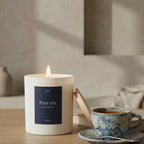 Bougie parfumée Pure thé JLT Bougies 220g allumée sur une table avec tasse de thé dans une ambiance douce et apaisante